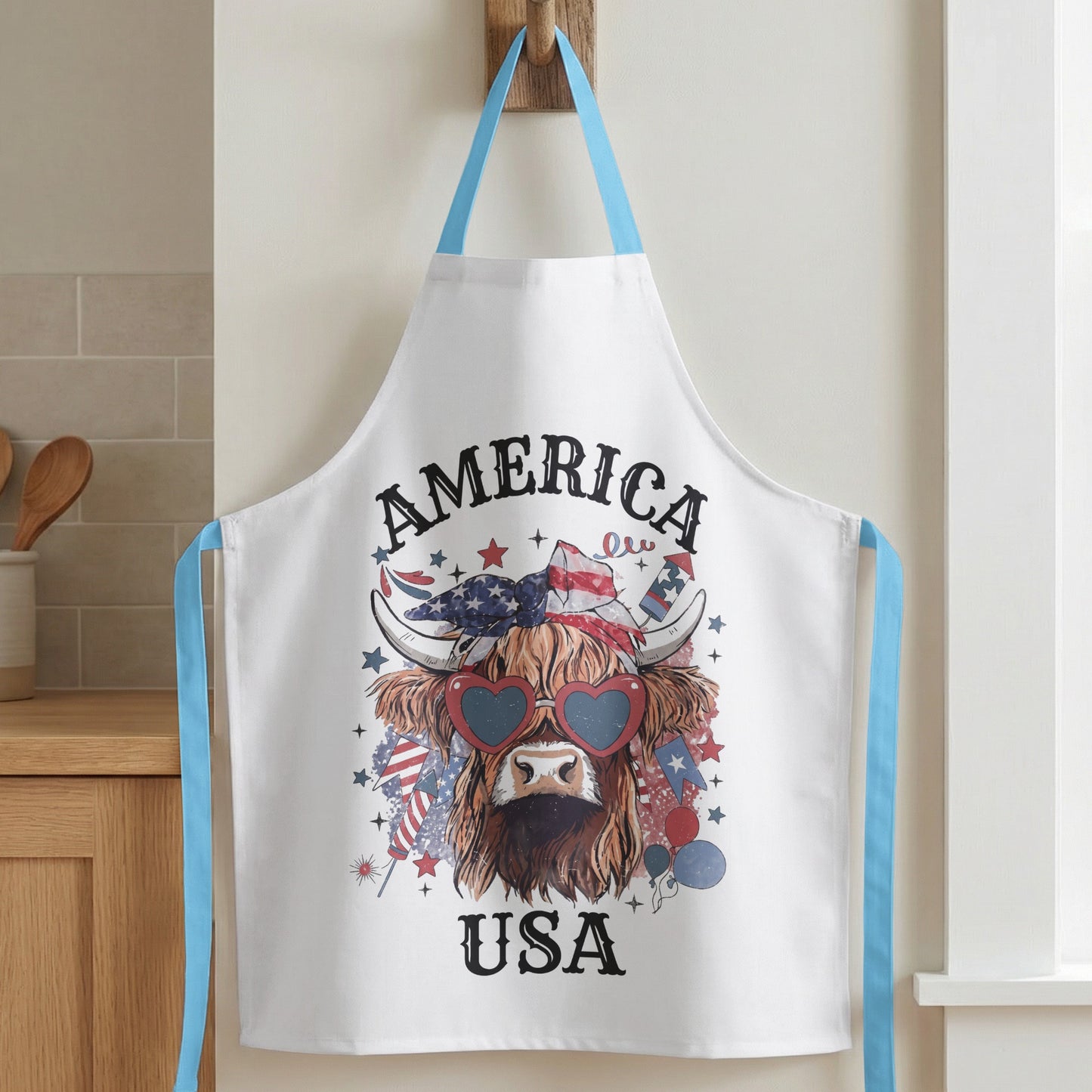 White apron with a distressed Highland cow graphic wearing heart-shaped sunglasses and patriotic bandana.
