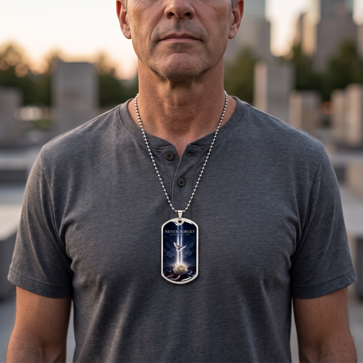 Man wearing the Never Forget 9/11 dog tag necklace with Tribute in Light, dove and white rose at an outdoor memorial at dusk