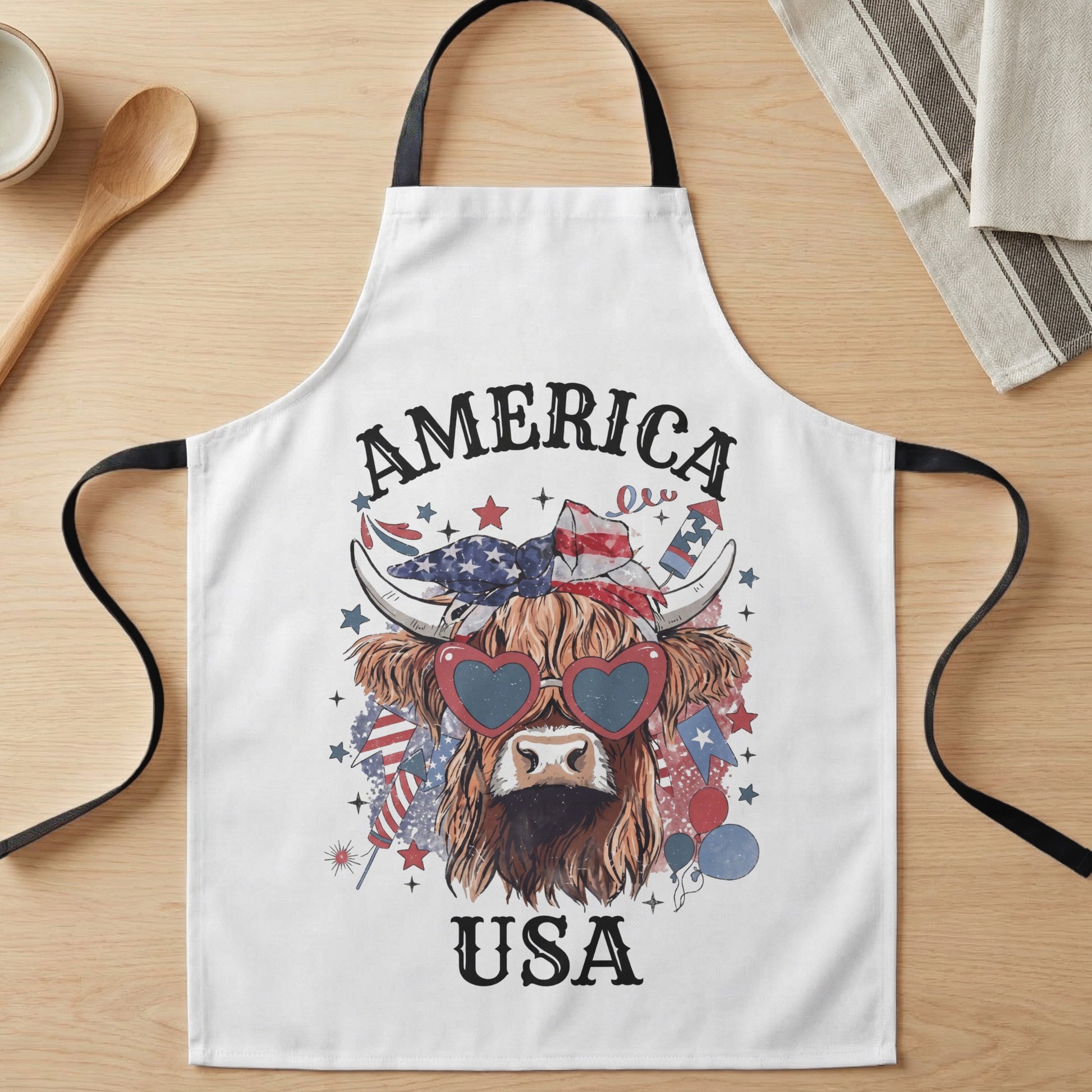 White apron with a highland cow wearing heart sunglasses, American flag bandana, and patriotic decorations.