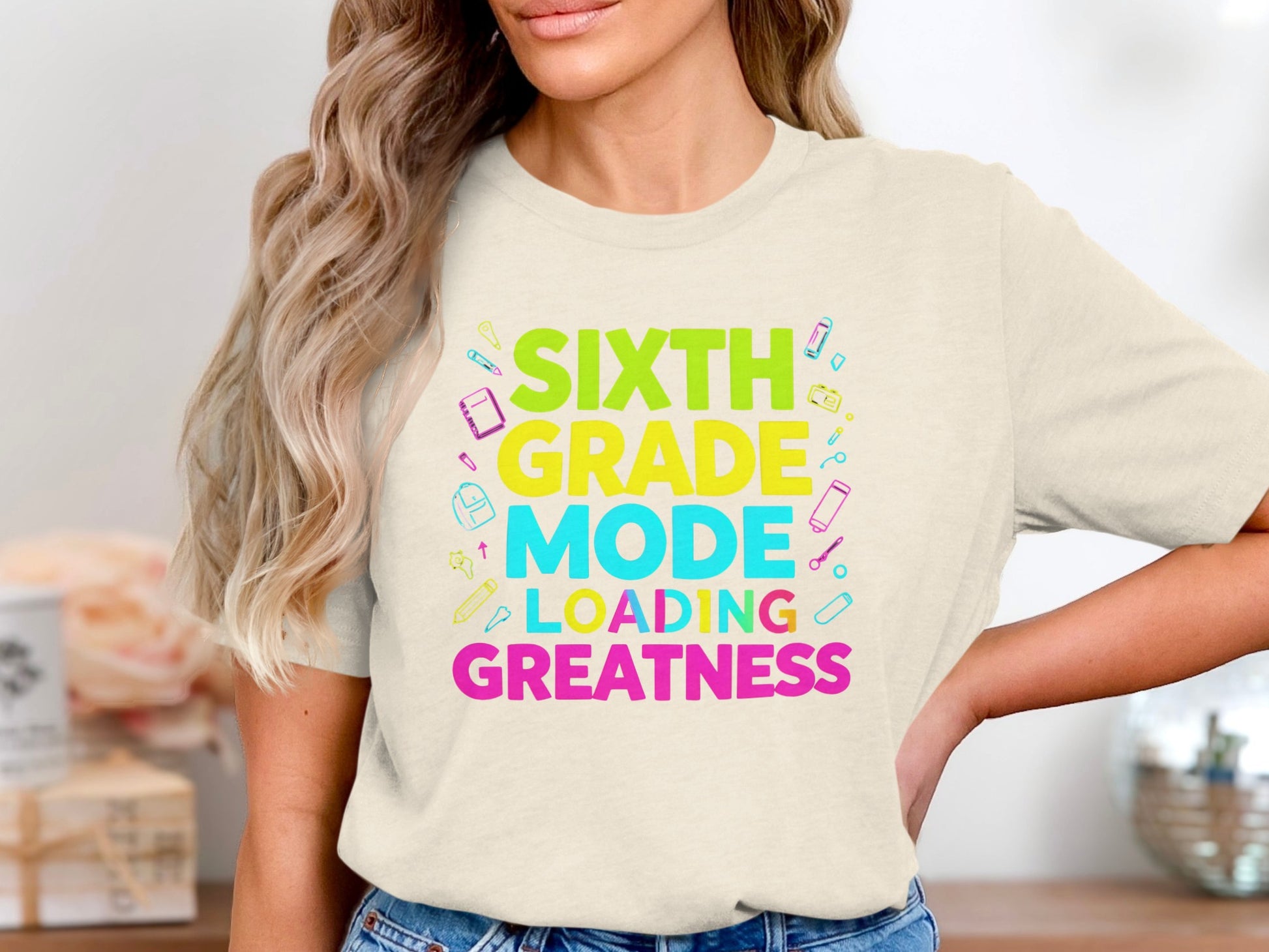 Sixth Grade Mode Loading Greatness tee with colorful school supplies.