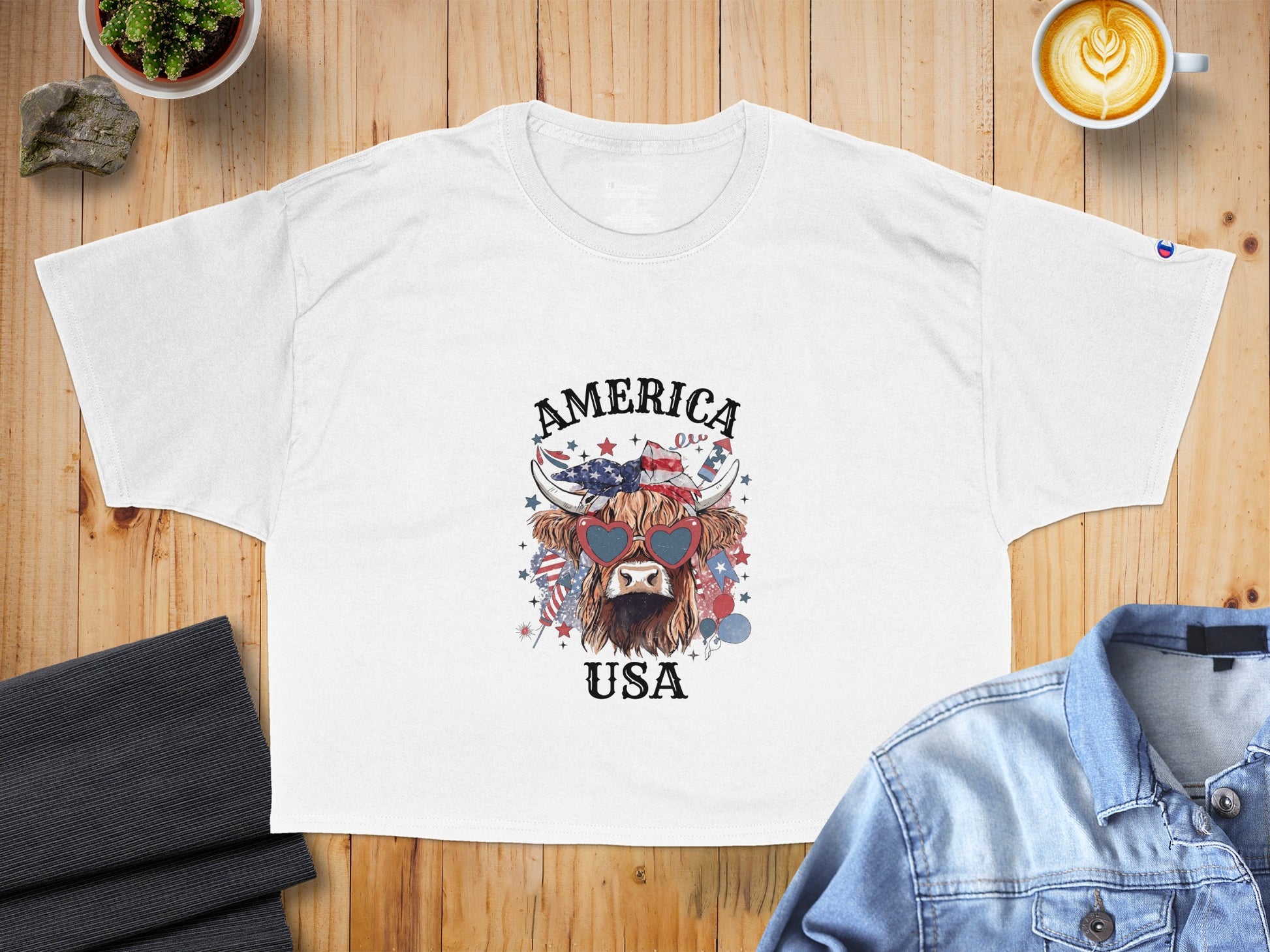 White t-shirt with a Highland cow graphic wearing heart sunglasses and patriotic USA elements.
