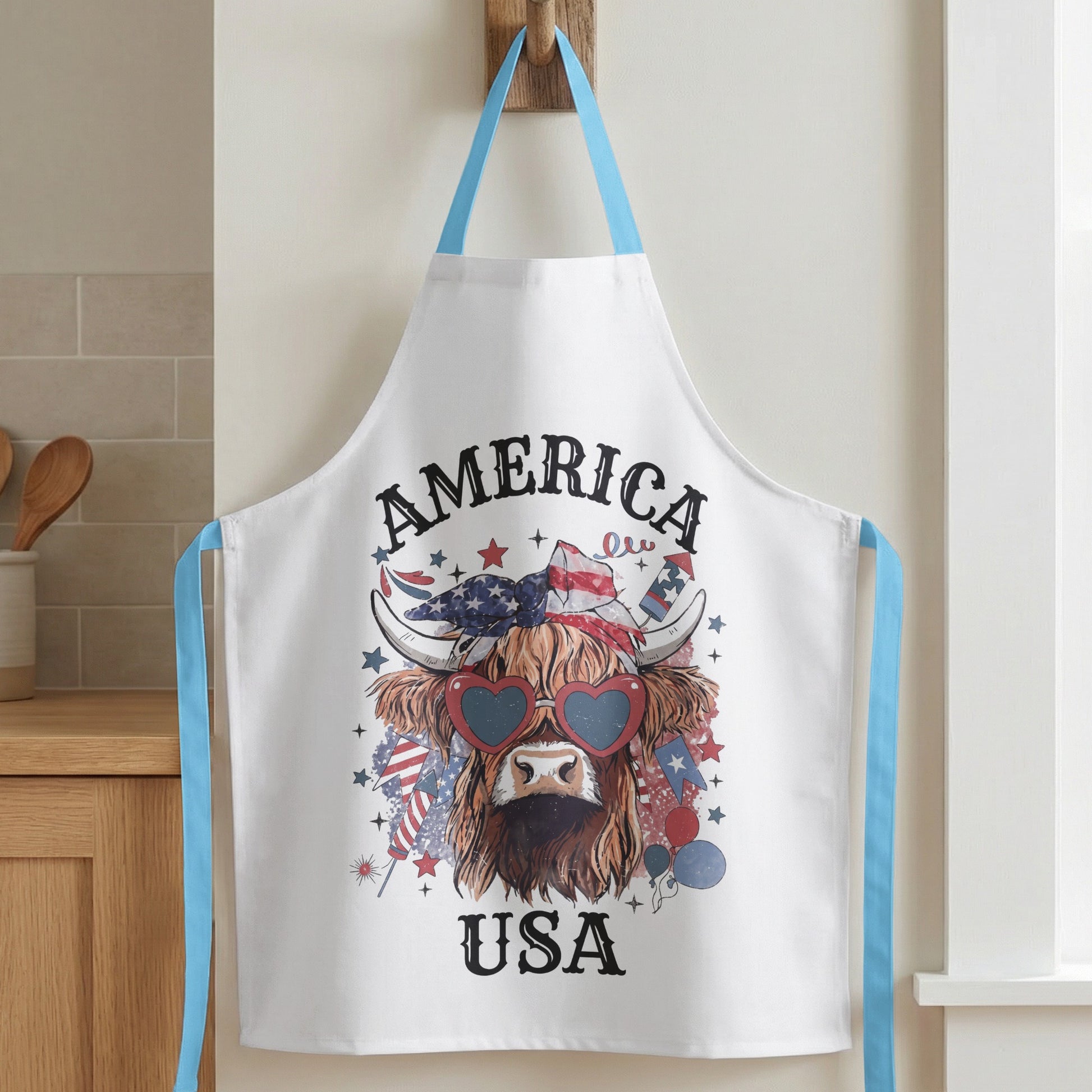 White apron with a distressed Highland cow graphic wearing heart-shaped sunglasses and patriotic bandana.