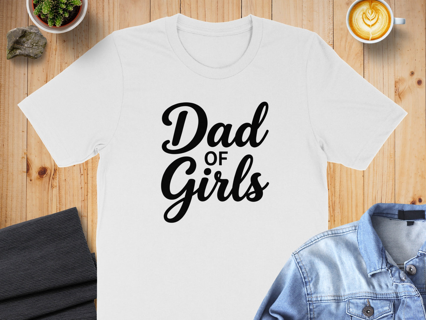White t-shirt with "Dad of Girls" text, laid flat with coffee and jeans.