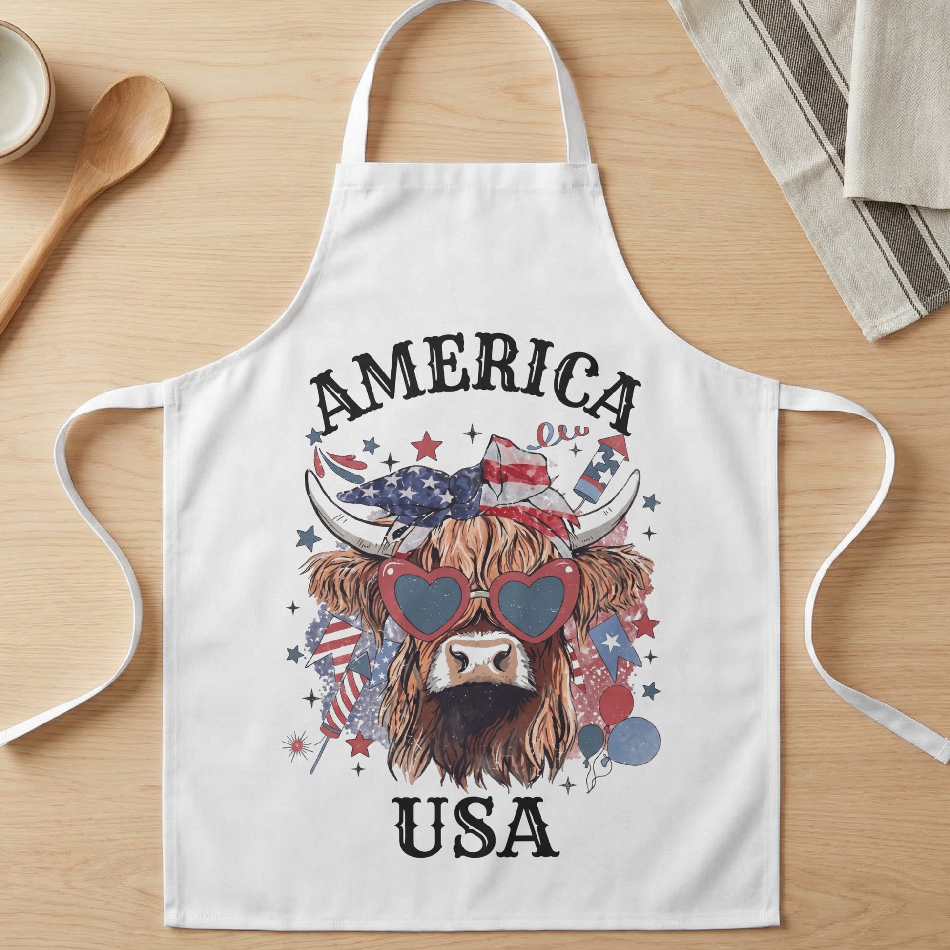 White apron with Highland cow wearing heart sunglasses and patriotic USA graphic.