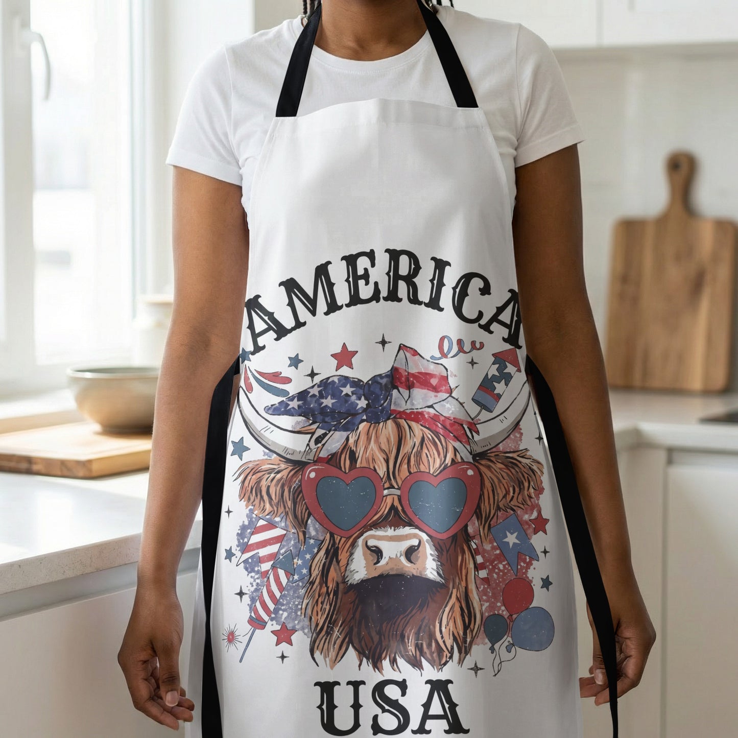 White apron with a Highland cow wearing heart sunglasses and an American flag bandana.