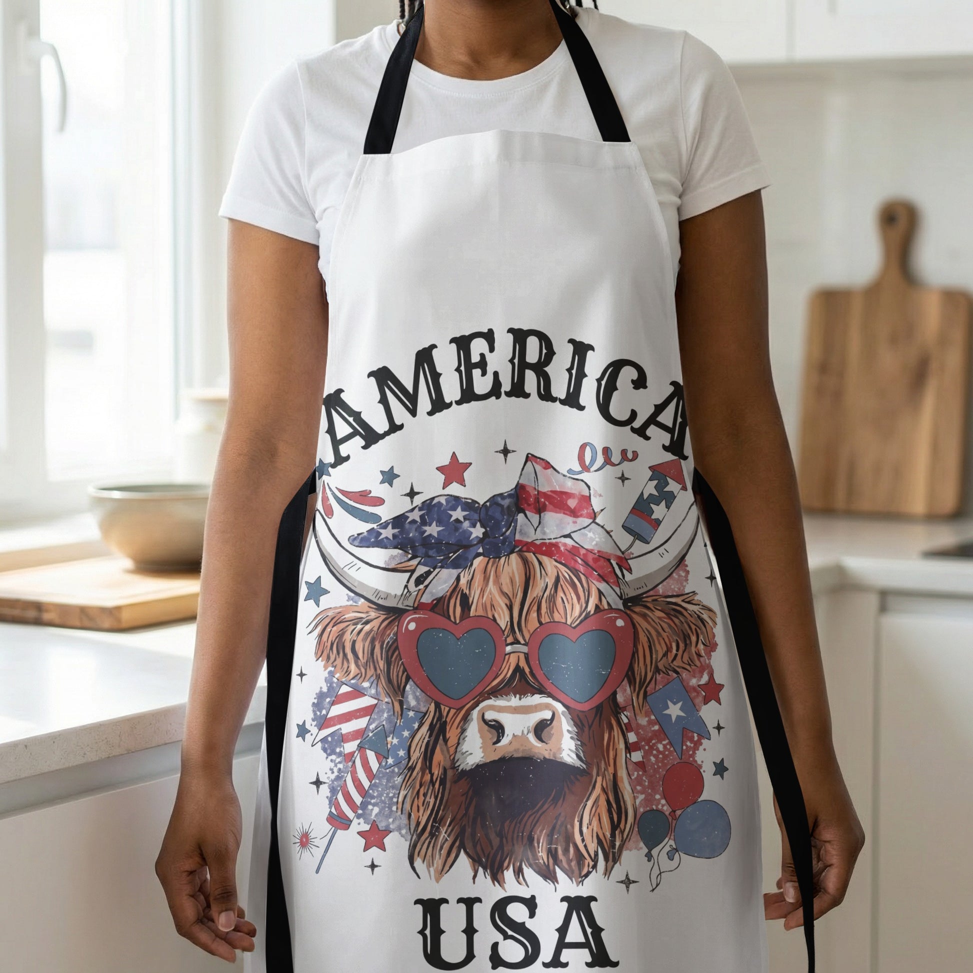White apron with a Highland cow wearing heart sunglasses and an American flag bandana.