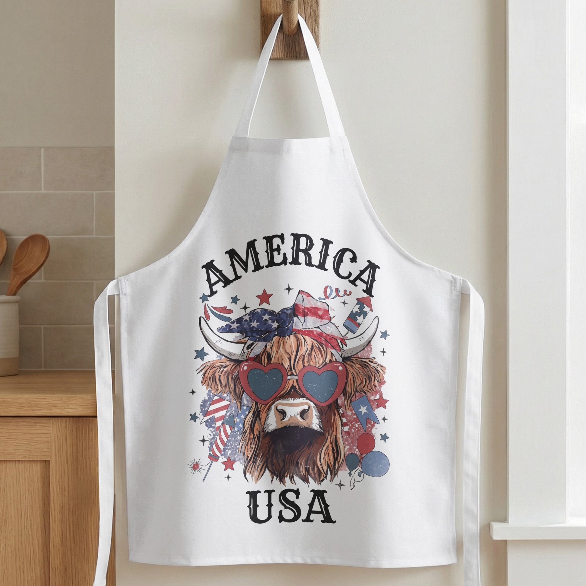 White apron with a Highland cow graphic wearing heart sunglasses and a bandana.