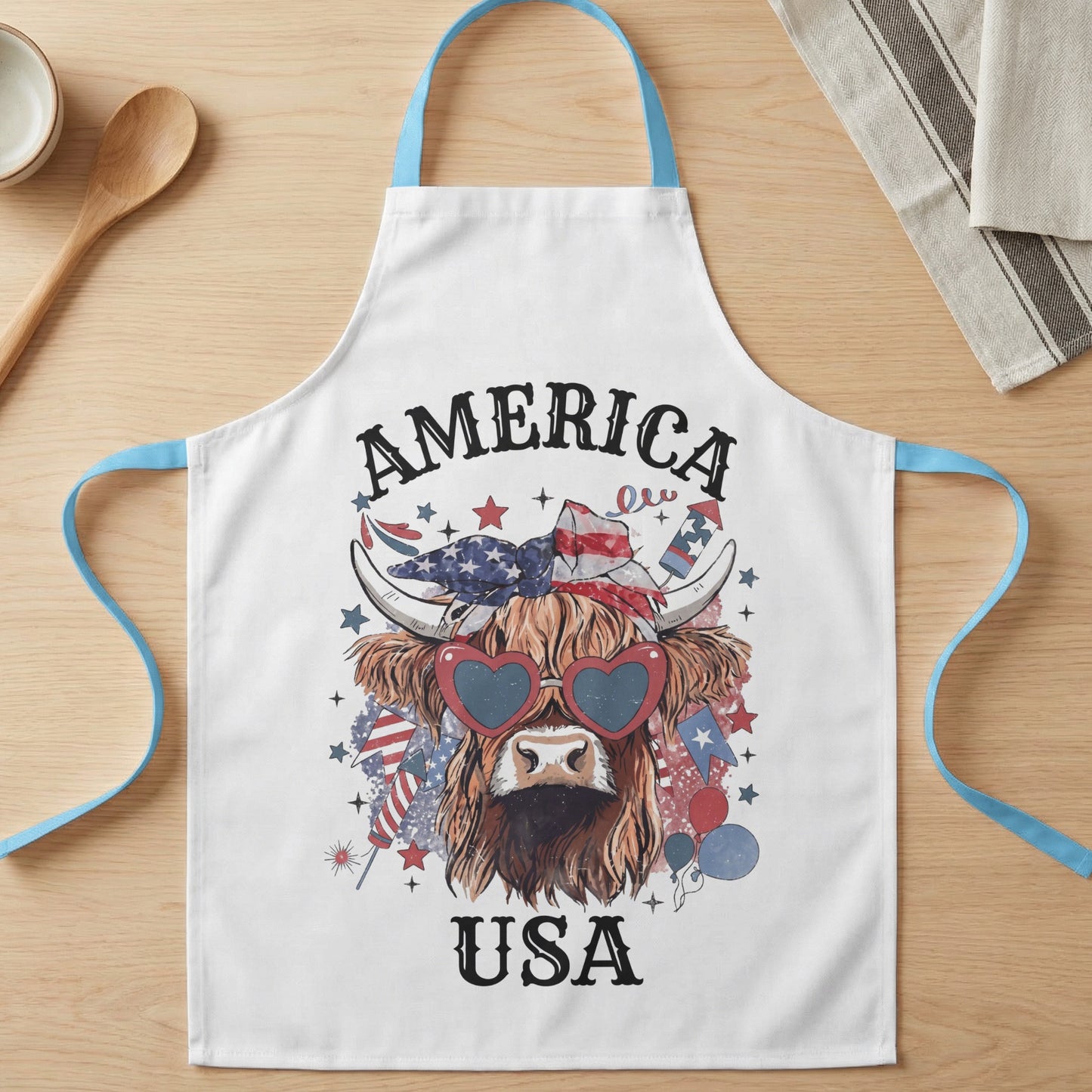 White apron with a highland cow wearing heart-shaped sunglasses, bandana, and "AMERICA USA" text.