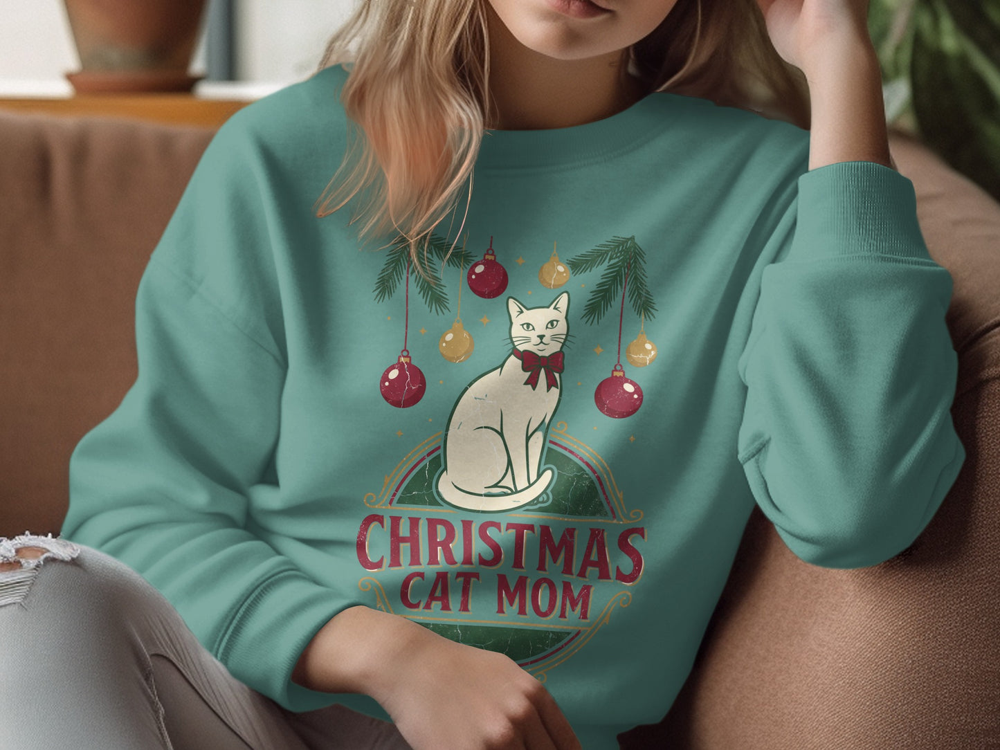 Light-colored cat with red bow under Christmas ornaments and text "Christmas Cat Mom."