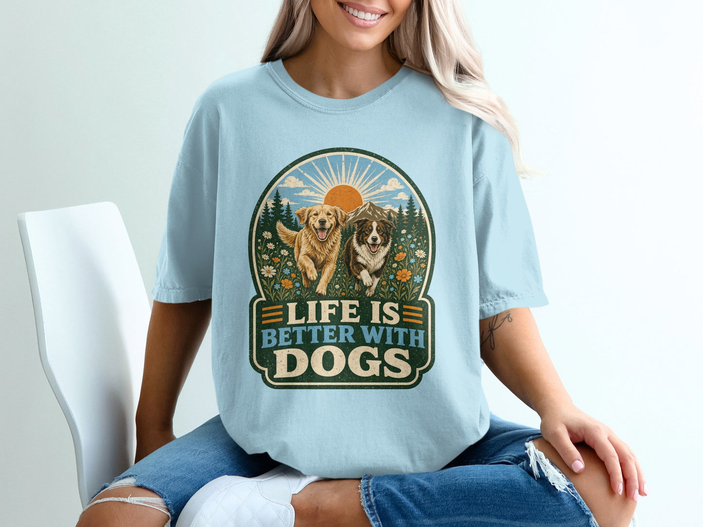 Light blue t-shirt graphic with two dogs, mountains, sun, and text "Life is Better with Dogs."