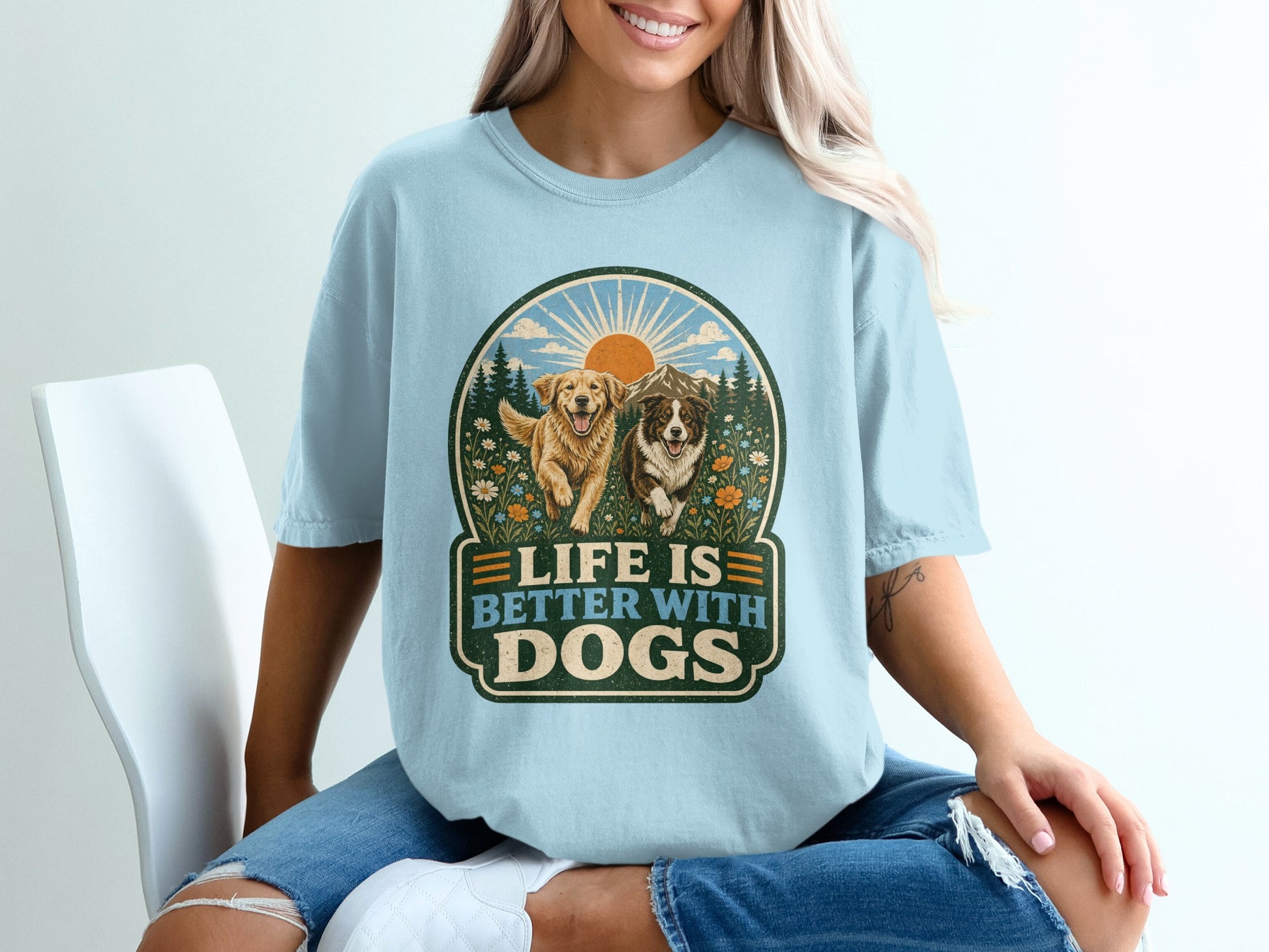 Light blue t-shirt graphic with two dogs, mountains, sun, and text "Life is Better with Dogs."