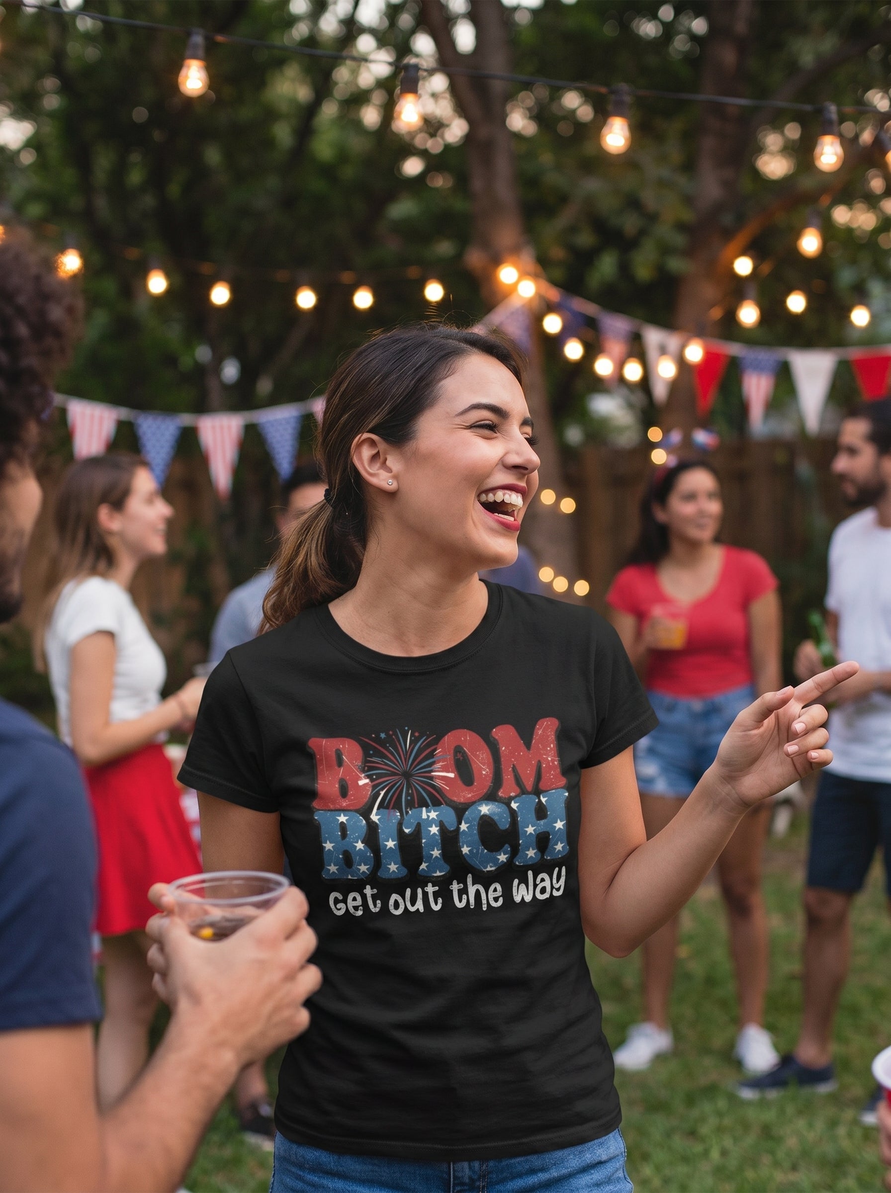 Lifestyle photo of woman wearing Bold Patriotic Boom B*tch T-Shirt at a 4th of July party