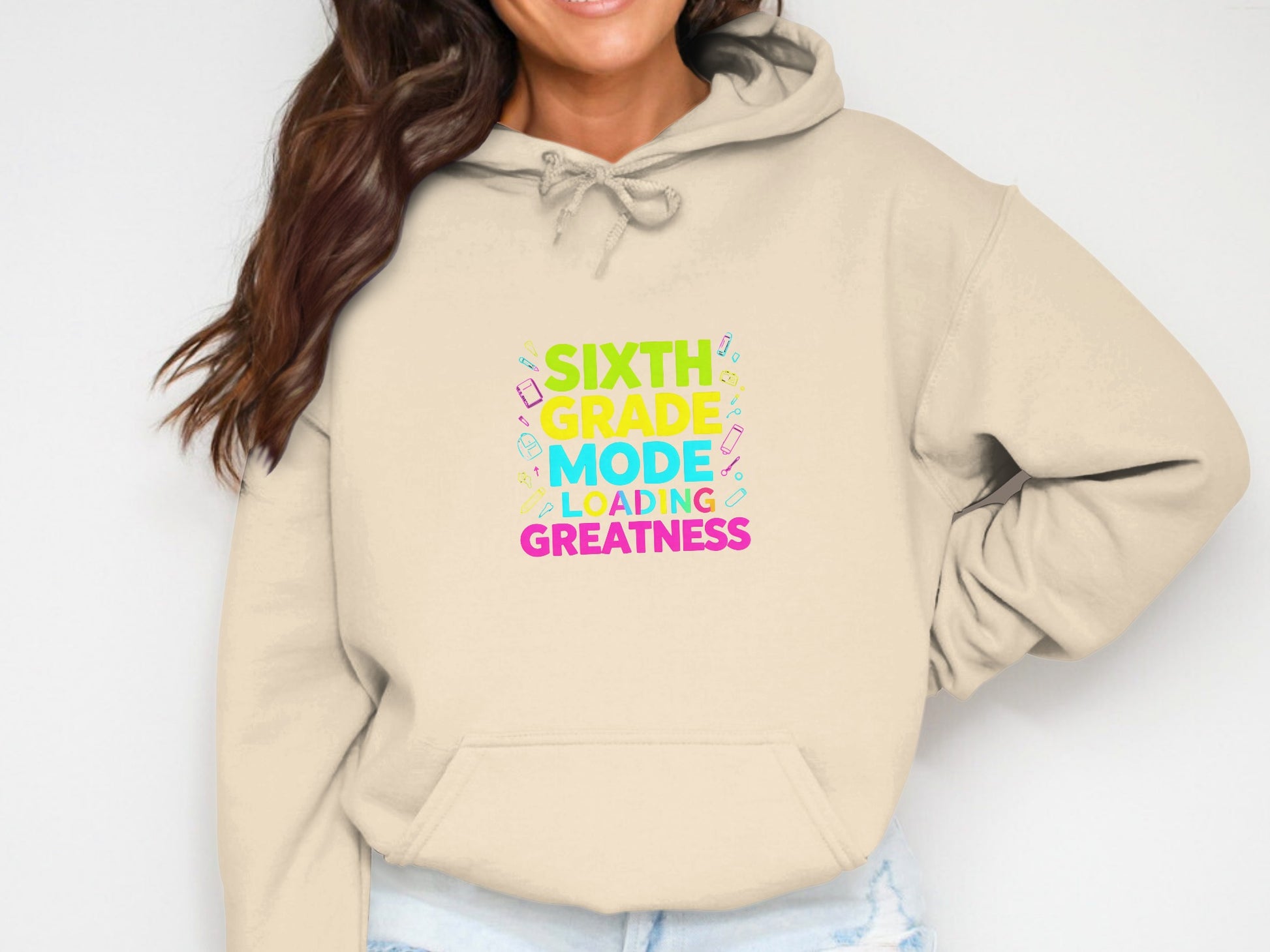 Cream hoodie with "Sixth Grade Mode Loading Greatness" text and school supplies graphics.