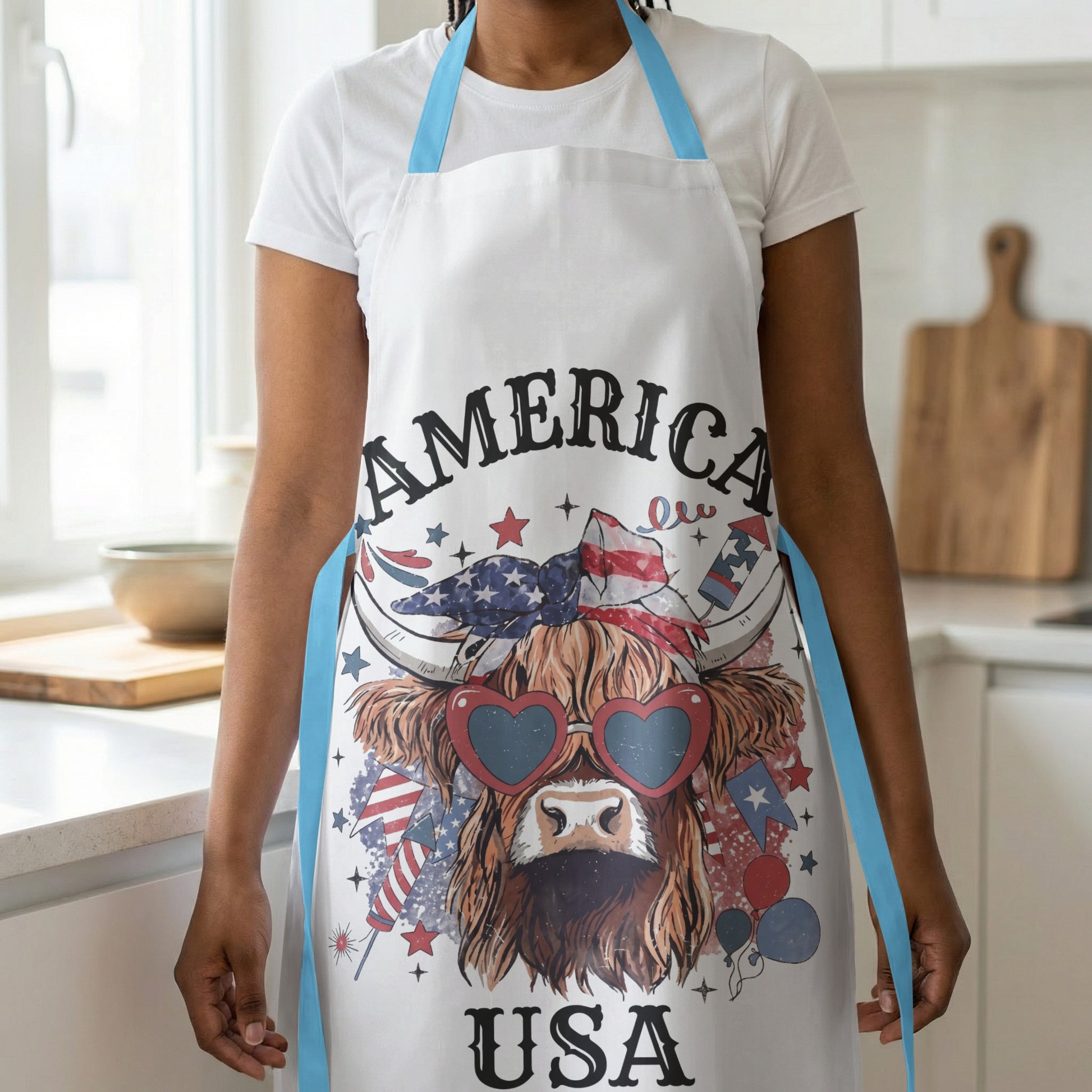 White apron with a Highland cow wearing heart sunglasses and American flag elements.