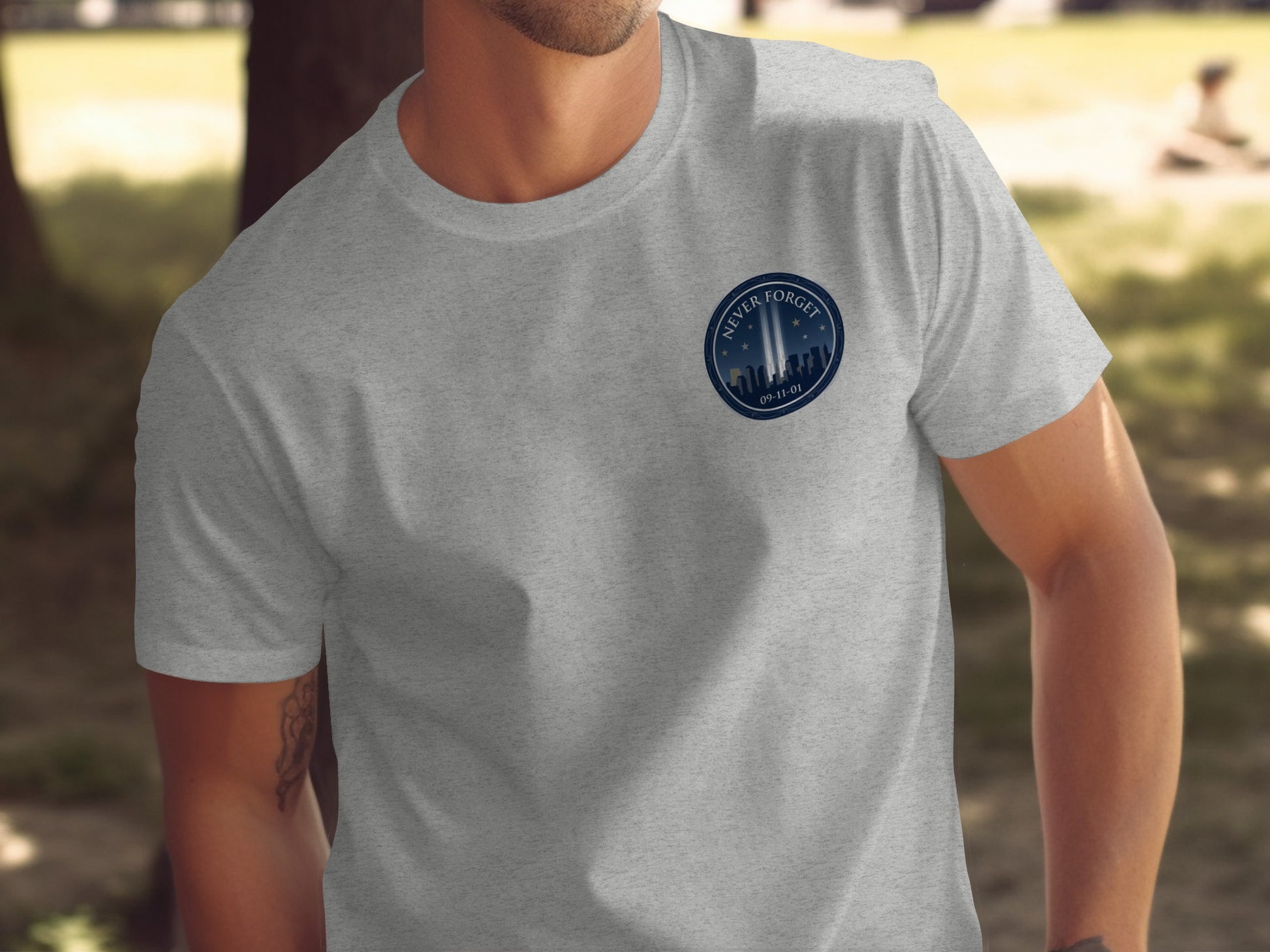 Grey t-shirt with a circular patch depicting the Tribute in Light and the text "Never Forget 09-11-01".