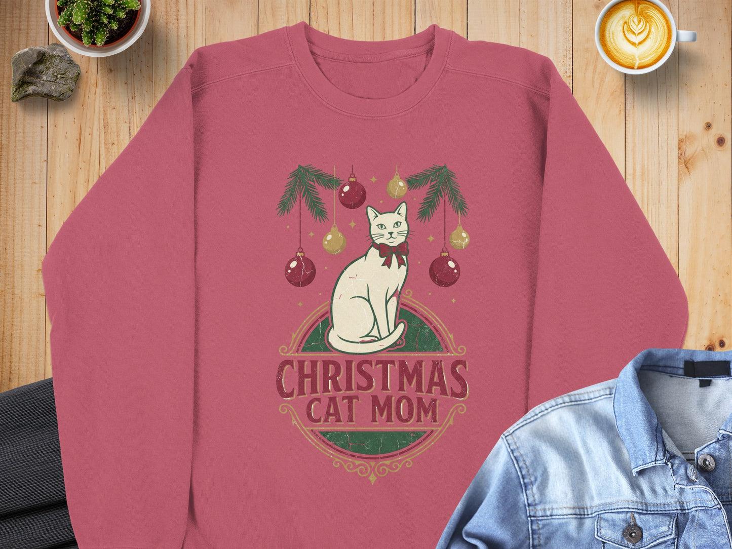 Pink sweatshirt with a graphic featuring a white cat, Christmas ornaments, and the text "CHRISTMAS CAT MOM".
