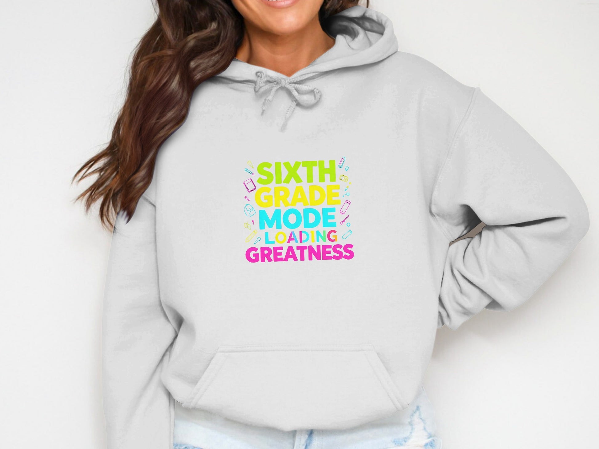 White hoodie with "Sixth Grade Mode Loading Greatness" text and school supplies graphics.